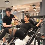 パーソナルトレーナーの指導でマシントレーニングを行う女性