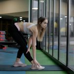 明るいジムの窓辺で下半身のストレッチをする女性