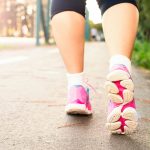 明るい道をスニーカーで歩く女性の足元