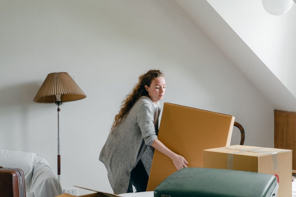部屋で大きな段ボール箱を持ち上げようとする女性