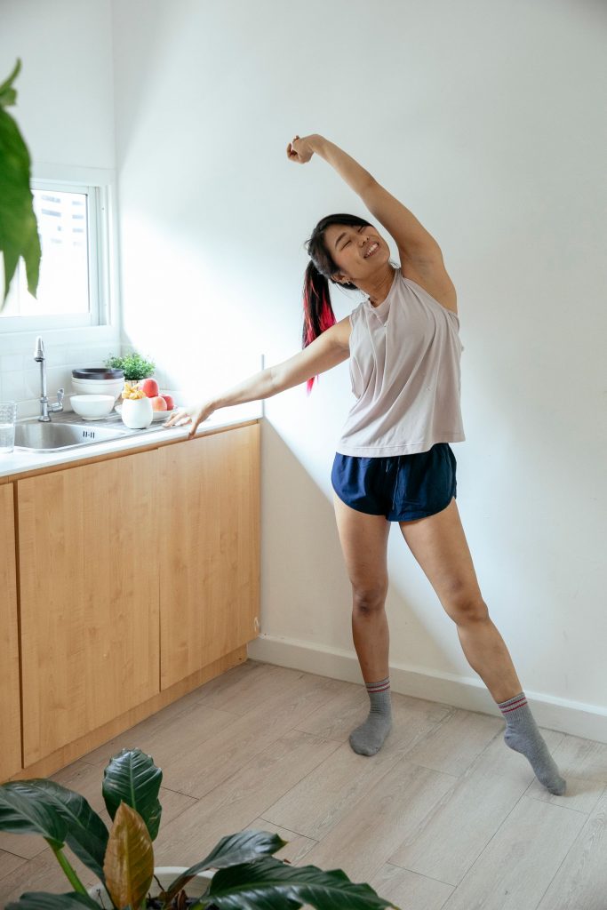自宅のキッチンで体の側面を伸ばすストレッチをする女性