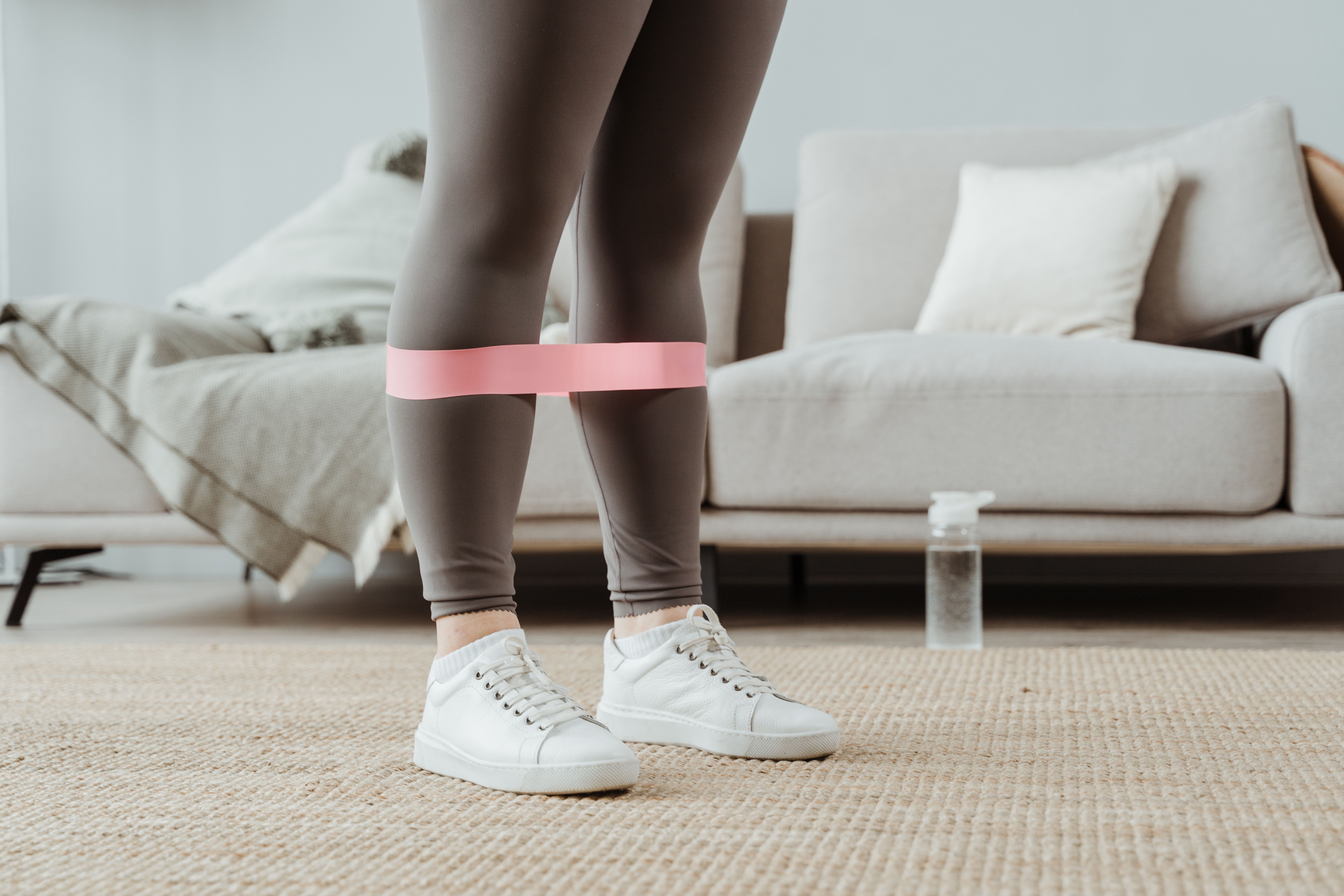 膝の上にトレーニング用のバンドを巻いて立つ女性の脚。自宅でのセルフケアのイメージ