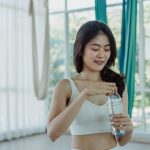 明るいスタジオで水のボトルを持つトレーニングウェアの女性