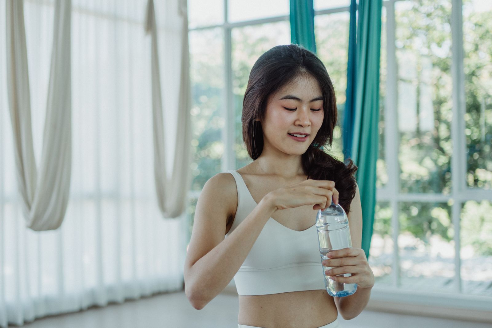明るいスタジオで水のボトルを持つトレーニングウェアの女性