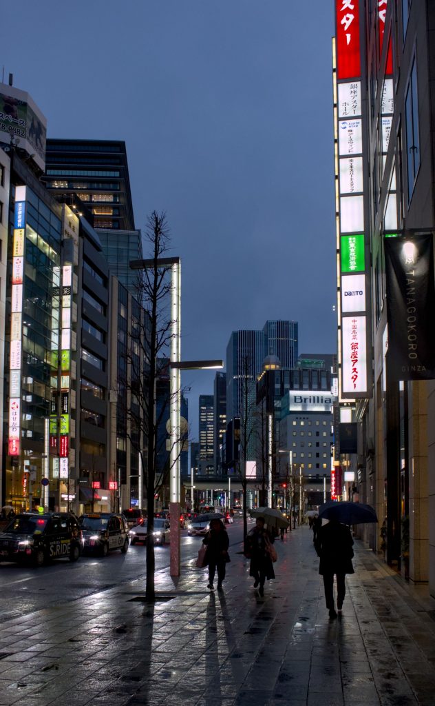 雨の日に傘を差して歩く人がいる夕方の街の通り