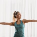 明るいスタジオで片脚立ちになり両腕を広げてバランスをとる女性