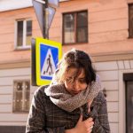 冬の寒さでコートの前を押さえ、肩をすぼめて歩く女性