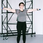 明るいスタジオで軽いダンベルを持ち両腕を広げる40代女性
